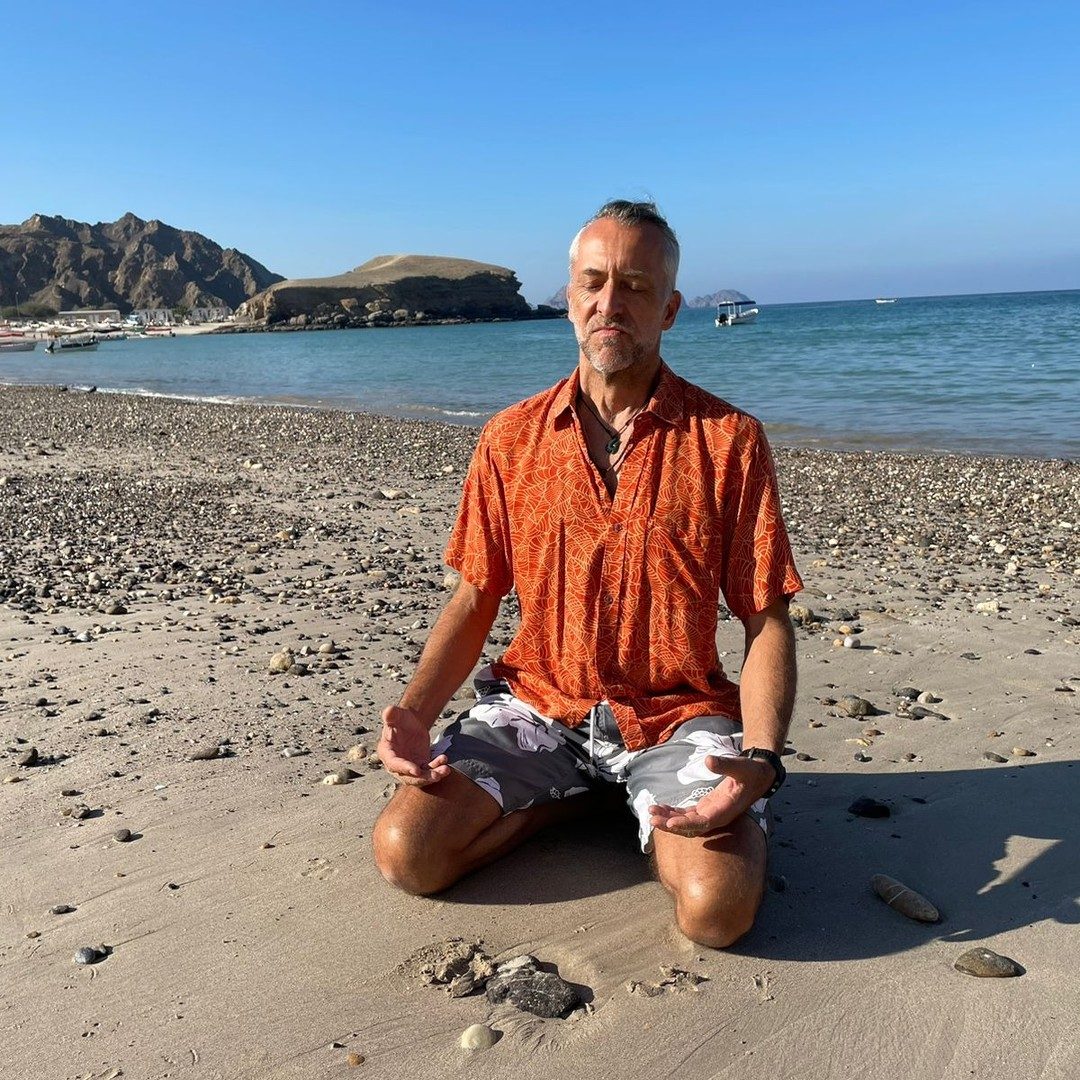 Thomas sitting cross-legged on a beach near Muscat